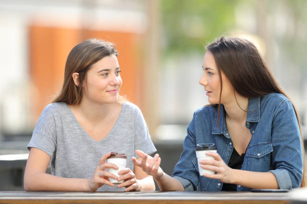 Two women holding coffee cups chat at a table.
